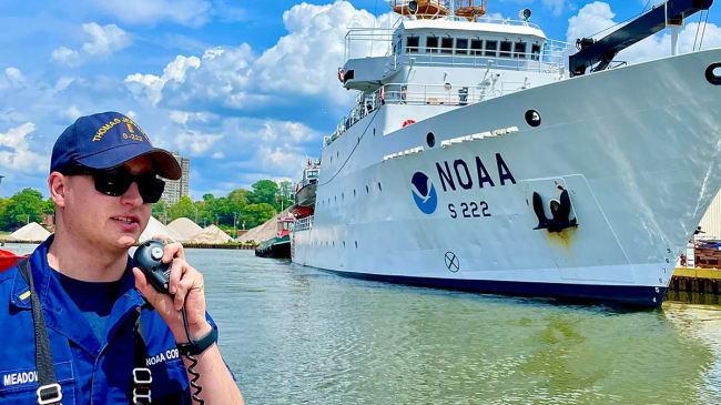 A NOAA survey vessel next to a dock along with a NOAA Corps officer in foreground.